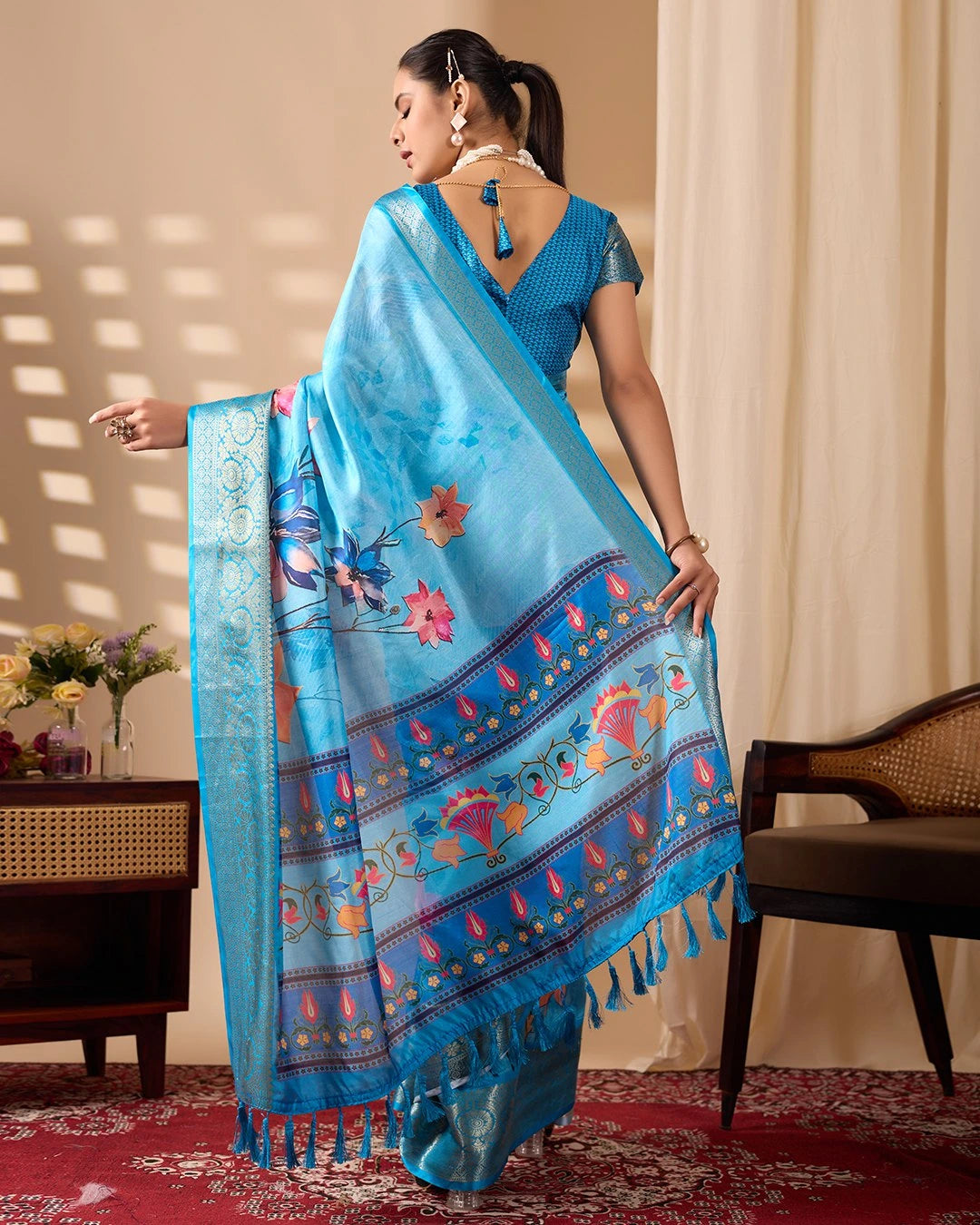 Woman wearing a blue saree with floral patterns in a room setting.